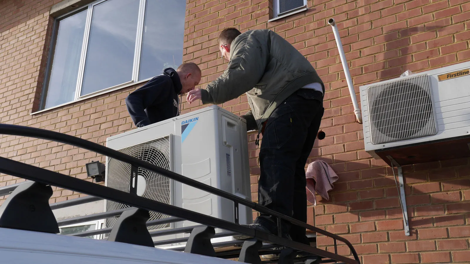 Deux techniciens VDV installent une unité extérieure en façade