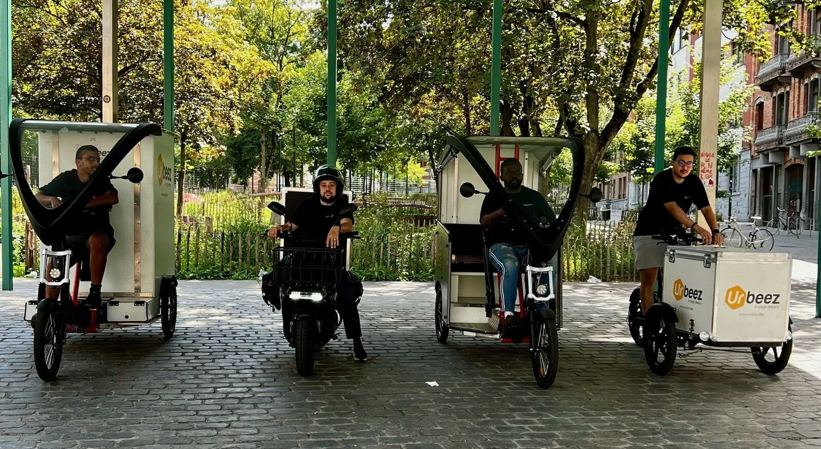 Koeriers van Urbeez met elektrische bakfietsen en een scooter op een Brussels plein