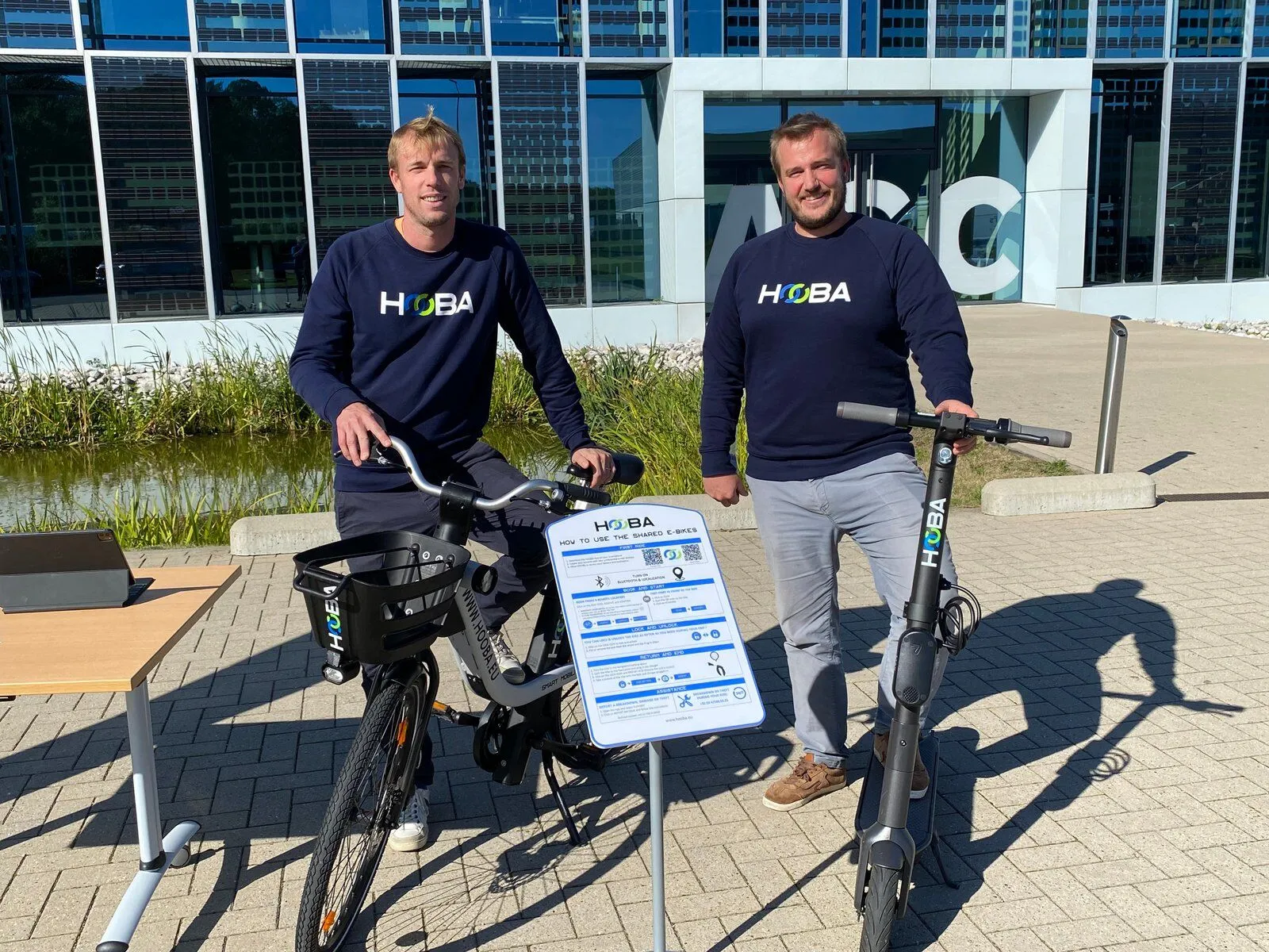 De oprichters van HOOBA, Serge en Adrien Devillers, met een gedeelde fiets en step