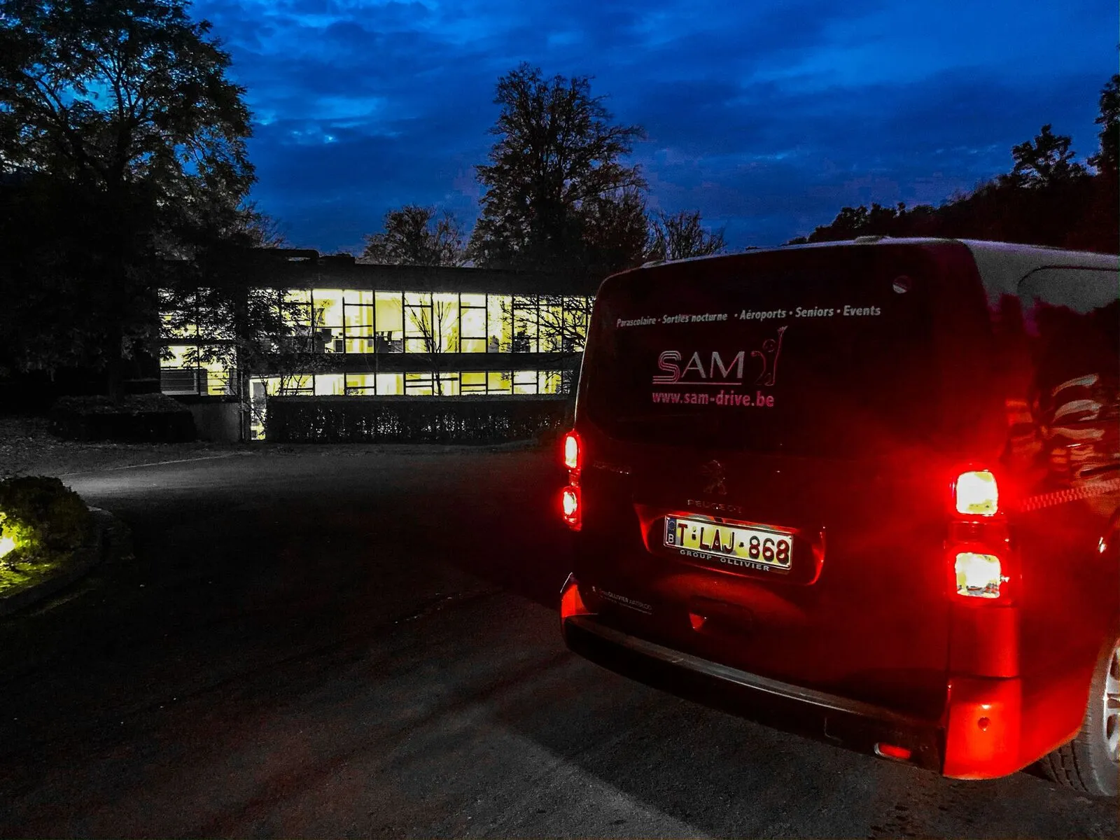 Un van SAM-Drive qui attend devant un bâtiment en soirée