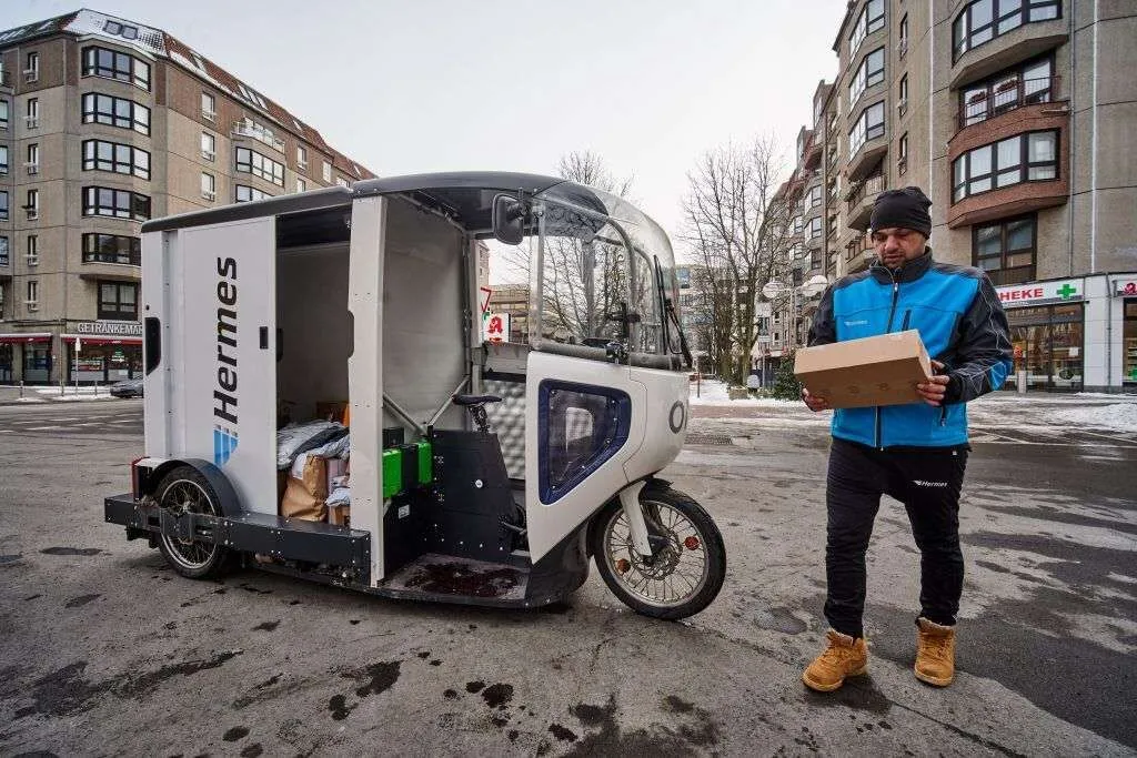 Een koerier levert een pakje af vanuit een ONO-bakfiets in een stadsstraat