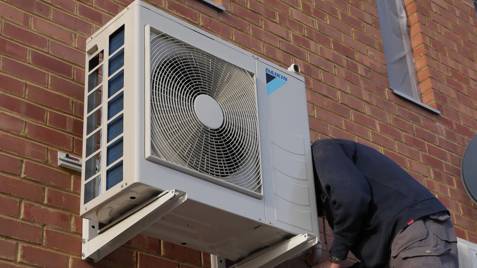 Technicien VDV fixant une unité extérieure Daikin sur une façade en briques