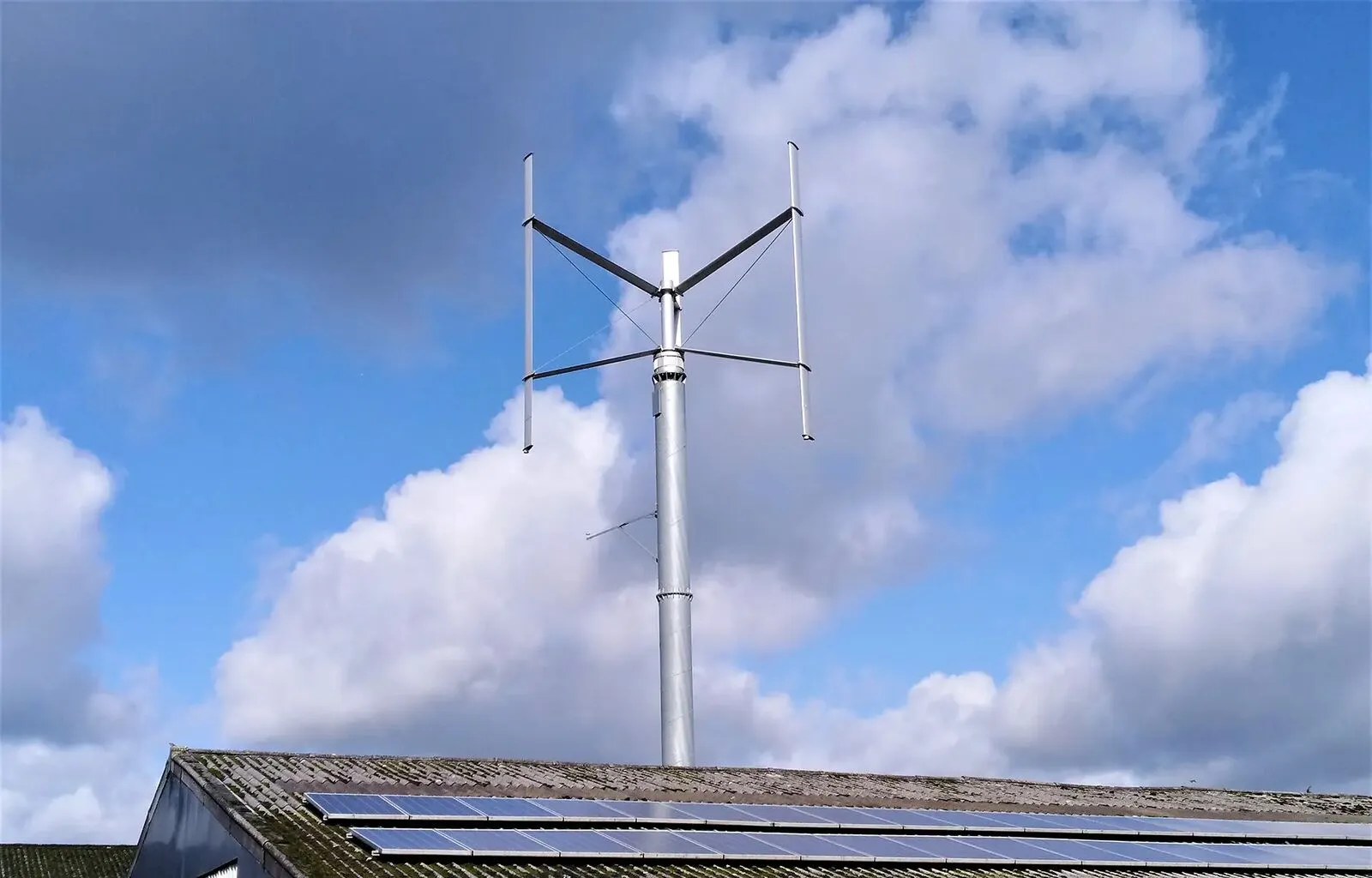 Éolienne à axe vertical au-dessus d'une toiture équipée de panneaux solaires